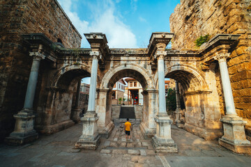 Obraz premium Hadrian's Gate. The three gates that are the symbol of Antalya. A man walks towards the gates. Wide angle photo taken on a cloudy day. Turkey.