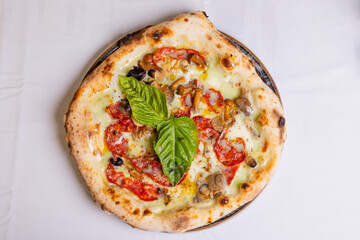 Pizza tradizionale napoletana con salame piccante, funghi, mozzarella e basilico fresco servita in una pizzeria elegante