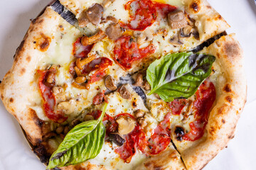 Pizza tradizionale napoletana con salame piccante, funghi, mozzarella e basilico fresco servita in una pizzeria elegante