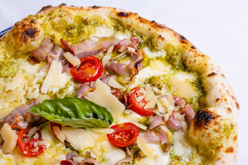 Pizza tradizionale napoletana con pesto di basilico, mozzarella, scaglie di formaggio, pomodori, pancetta croccante e basilico fresco servita in una pizzeria elegante