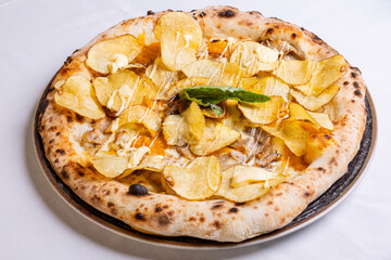 Pizza tradizionale napoletana con mozzarella, porchetta, chips di patate fritte, crema di formaggio e basilico fresco servita in una pizzeria