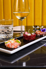 Tre tartare di pesce fresco servite come antipasto in un ristorante di pesce elegante con un calice di vino bianco d'accompagnamento