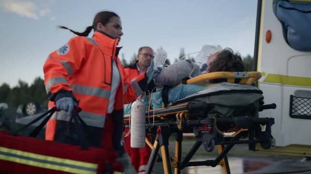 Car Crash Traffic Accident: Team of Paramedics and Firefighters Rescue Injured Person in Rollover Vehicle. Emergency Medical Professionals Provide First Aid as Firemen Extinguish Fire. Slow Motion