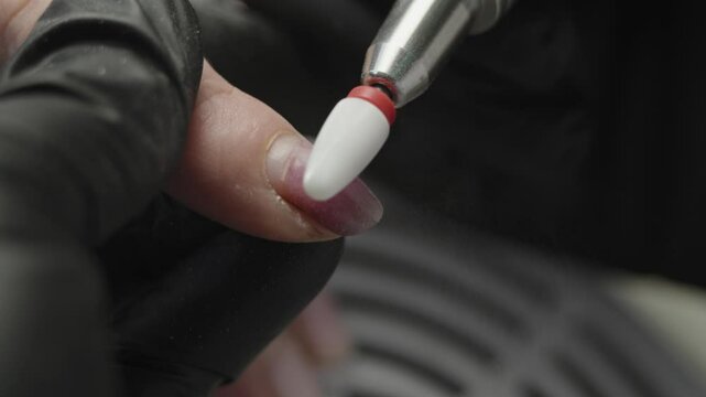 A woman manicure master makes a hardware manicure in black gloves removing the old coating of gel Polish in the salon. The concept of beauty professional nail care