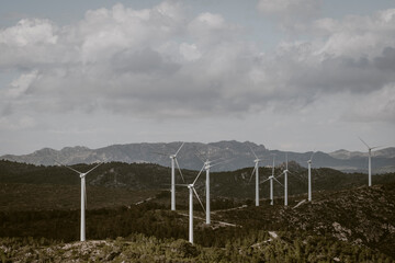 Numerous wind turbines are scattered across a mountainous terrain under a cloudy sky, demonstrating the intersection of technological advancement and natural landscapes in Tarragona Spain