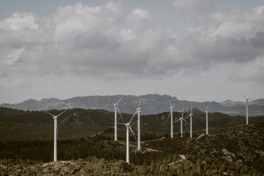 Numerous wind turbines are scattered across a mountainous terrain under a cloudy sky, demonstrating the intersection of technological advancement and natural landscapes in Tarragona Spain