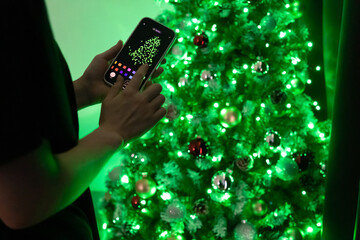 Christmas tree lights through smart home app. Green Christmas tree. Girl customizing garland. Smart home. Painting a Christmas tree through the app.