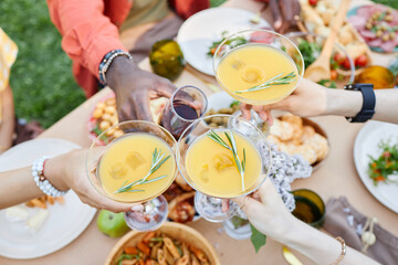 Friends toasting with cocktails during an al fresco dining experience, celebrating togetherness and sharing laughs around a table filled with assorted dishes and appetizers