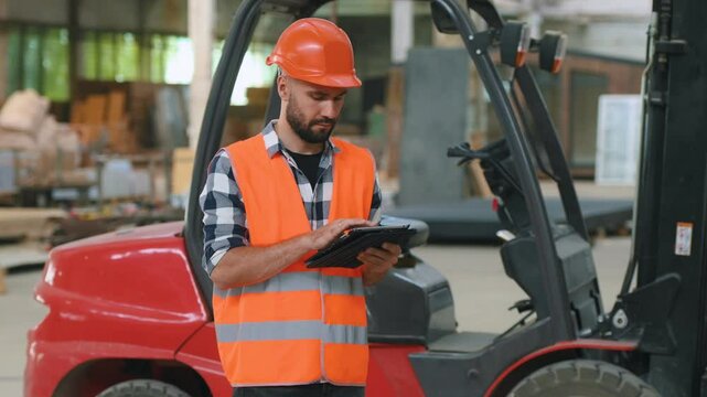 Caucasian Male Stocking Associate Doing Inventory On Tablet, Checking Delivery Tracking Number On Boxes. Man Working In Warehouse Facility With Conveyor Belt Packing Products For Online Customers.