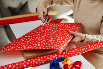 Female hands are cutting wrapping paper. Packaging gifts for the celebration. Gift wrapping in red...