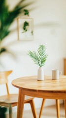 Fototapeta premium A small white vase with palm leaves and a white cup sit on a wooden table in a soft-focus minimalist interior.