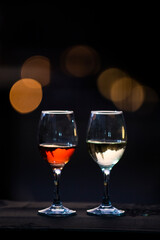 Two partially filled wine glasses with red and white wines sitting on a shelf with twilight bokeh.