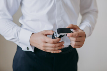 A man is wearing a white shirt and black pants. He is holding a watch in his hand
