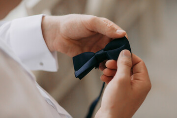 A man is holding a black bow tie in his hand. The bow tie is tied and ready to be worn