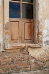 Window in old building ruin with crumbling cement walls revealing the brick structure.