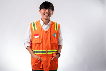 An Asian man wears an orange safety vest with reflective stripes and the Indonesian flag on the pocket. He smiles confidently, standing against a plain white background, representing safety