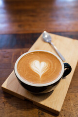 Latte coffee or cappuccino coffee in black cup with beautiful heart latte art on wooden table.