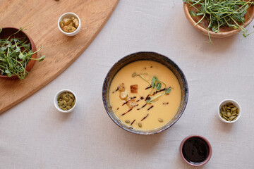 Minimal top view of sophisticated bowl of cream soup with cheese or pumpkin and different add ons on white restaurant table copy space