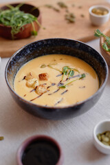 Vertical close up of delicious cheese or pumpkin cream soup in dark stone bowl on table with rustic setup