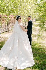 Fototapeta premium A bride and groom are walking in a field with a white dress and a black suit. The bride is holding a bouquet and the groom is holding her hand