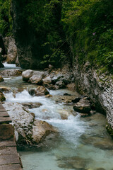 a small mountain stream flowing through a narrow gorge surrounded by steep cliffs and dense vegetation. The water in the stream is clear and stormy, it flows over the rocks, creating white foam. On th