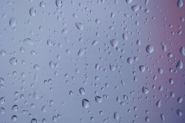 vista macro frontale di gocce di pioggia su un vetro trasparente, con sfondo astratto dalle sfumature miste viola e grigio chiaro