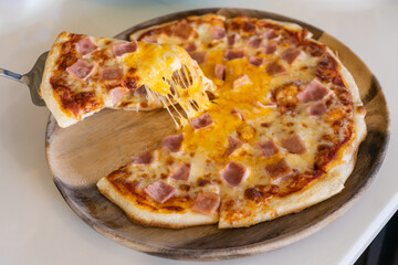 Close-up taking piece of pizza.  Cheese pizza with ham slices. Home and  office delivery concept