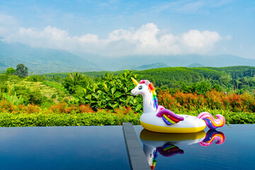 Unicorn swim tube on the swimming pool with garden and mountain background