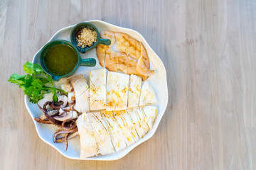 Grilled squid served with seafood sauce in a white plate on a wooden table.