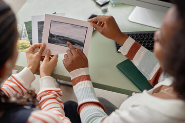 High angle closeup of two African American two women collaborating on creative project and holding photo prints with nature landscapes