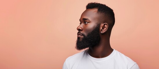 A stylishly groomed African American man sporting short hair and a beard stands against a soft peach backdrop in a panoramic setting with room for text or images. Creative banner. Copyspace image