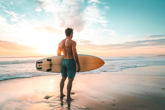 A male surfero stands on the beach holding a surfboard