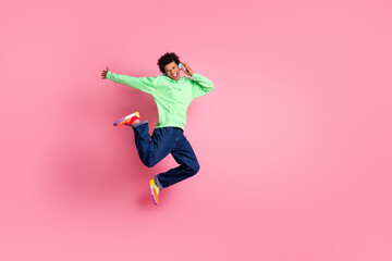 Full body portrait of cool young man jump headphones wear green hoodie isolated on pink color background