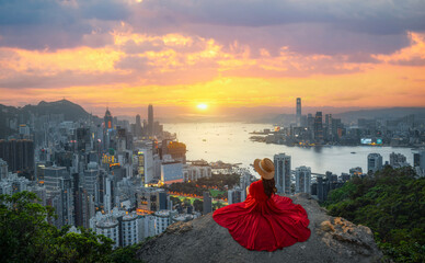 Asian woman enjoying beautiful view on top of Hong Kong city hill at sunset. Dusk skyscrapers over...
