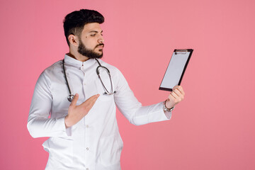 Side view of young, male dctor, intern standing, looking aside, holding folder, raising hand, showing. Concept of medicine.