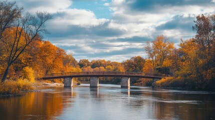 Fototapeta premium A bridge crossing a river, surrounded by autumn trees, with the sky overhead.