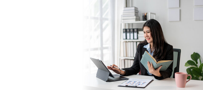 A woman is sitting at a desk with a laptop and a book