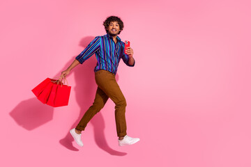 Full size photo of nice young man jump run phone bags empty space wear shirt isolated on pink color background