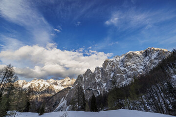 ampia vista panoramica su varie catene montuose innevate in alta montagna, nella Slovenia nord occidentale, di pomeriggio, a fine inverno, sotto un cielo azzurro, coperto da qualche nuvola bianca