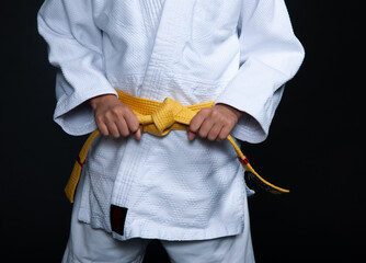 A young judoka in a white kimono ties a yellow belt
