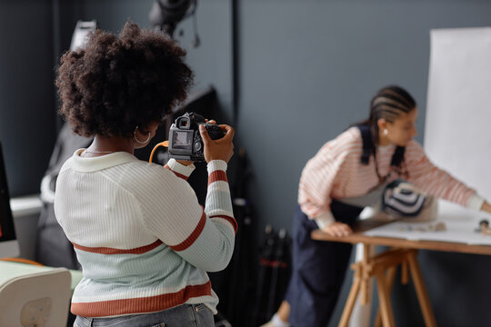 Back view of Black woman as female photographer taking pictures in photo studio during product photoshoot copy space