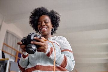 Candid low angle portrait of smiling Black woman as female photographer holding camera and looking at pictures on screen copy space