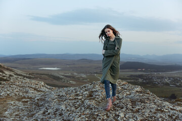 Obraz premium serene woman in green jacket and jeans standing on mountain top with hands in pockets