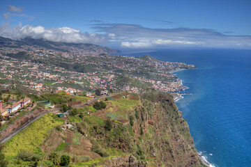 Madeiras Südküste mit der Steilküste im Vordergrund und der Hauptstadt Funchal im Hintergrund 