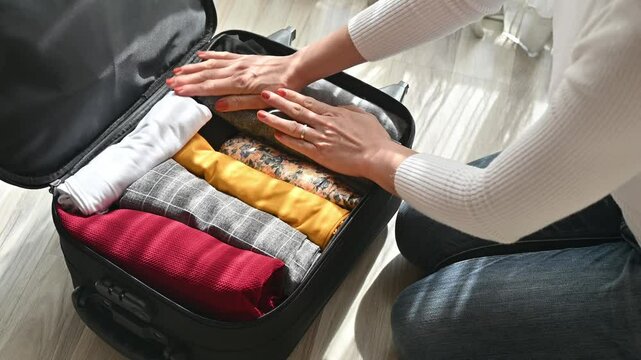 Footage of woman opening her suitcase for pack and arranging colorful clothing before traveling in holiday period.