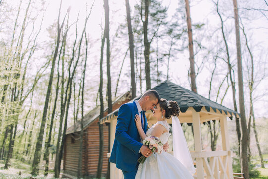 A bride and groom are standing in front of a wooden gazebo, with the bride holding a bouquet
