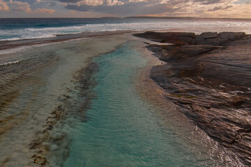 The sun sets over a rock pool that leads the way to the ocean
