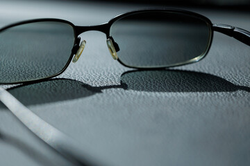vista macro di un paio di occhiali dalle lenti parzialmente scure appoggiate su una superficie liscia e uniforme © PhotoMet