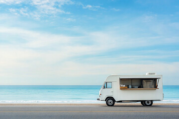 A white food truck, on the side of the road next to the sea.