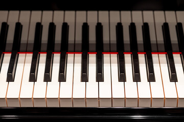 Keyboard of a grand piano in a concert hall with stage lighting. The black and white keys of the elegant musical instrument form a strong contrast and are reflected in the high-gloss lacquer. © ON-Photography